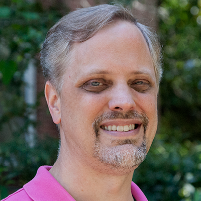 Robert Foster smiling at the camera, wearing a pink polo