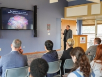 photo of man speaking, with screen, audience