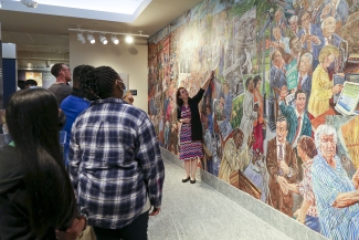 photo of students, with mural and woman pointing