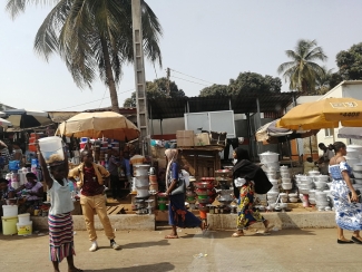 Photo of outdoor marketplace with goods, umbrellas, people and palm trees