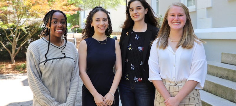 photo of four women, outdoors, building in background