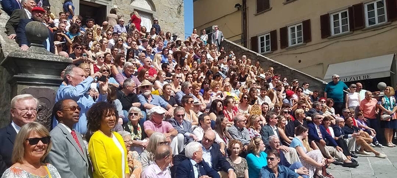 photo of a large group seated on sunny steps of a medieval palace.