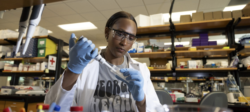 photo of woman working in lab with pipette, gloves, safety glasses