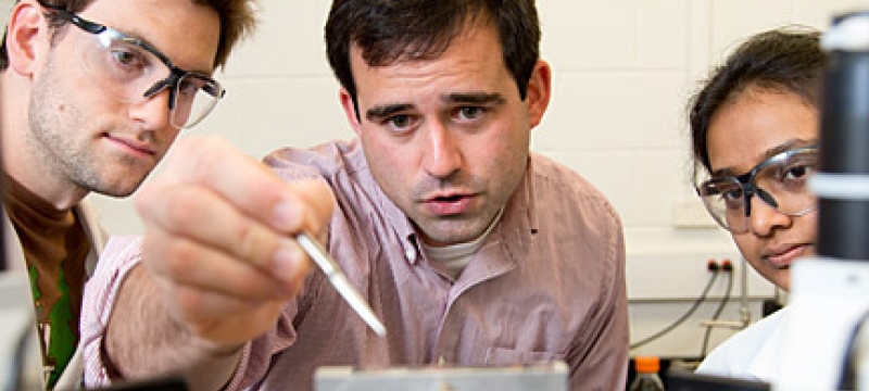 professor in lab, flanked by two students