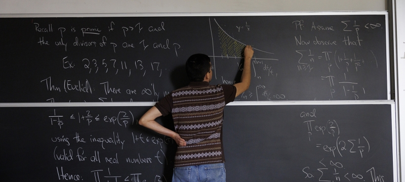 photo of person writing on chalkboard, back turned