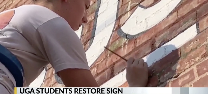 photo of woman painting letters on exterior brick wall