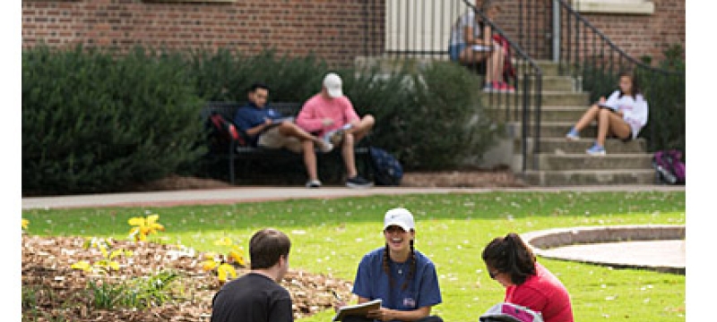 students sitting ton the ground in front of brick building