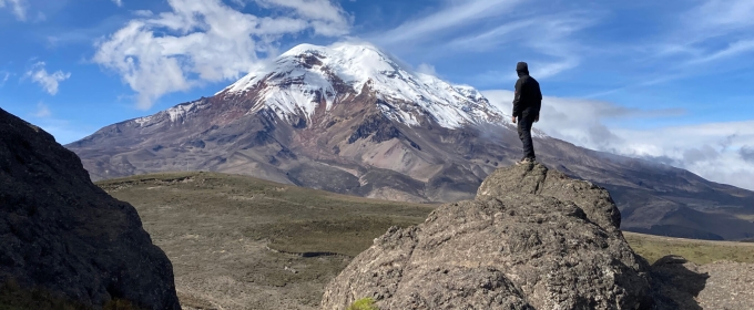 photo of man standing on rock looking at mountain, day