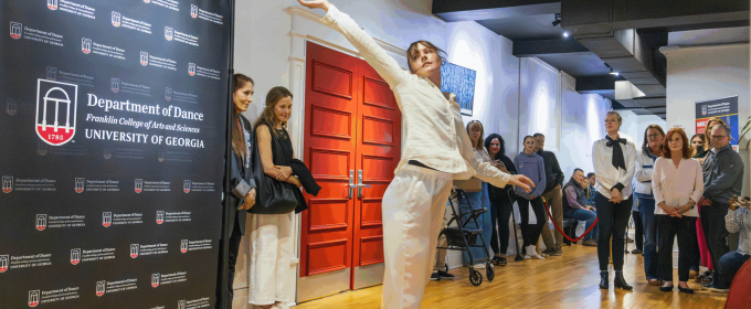 woman dances in room, people and banner in background.