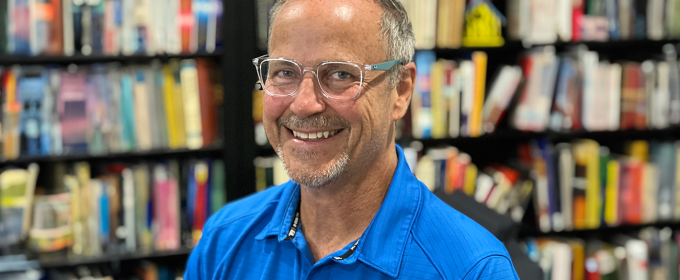 photo of man, bookshelves and books in background